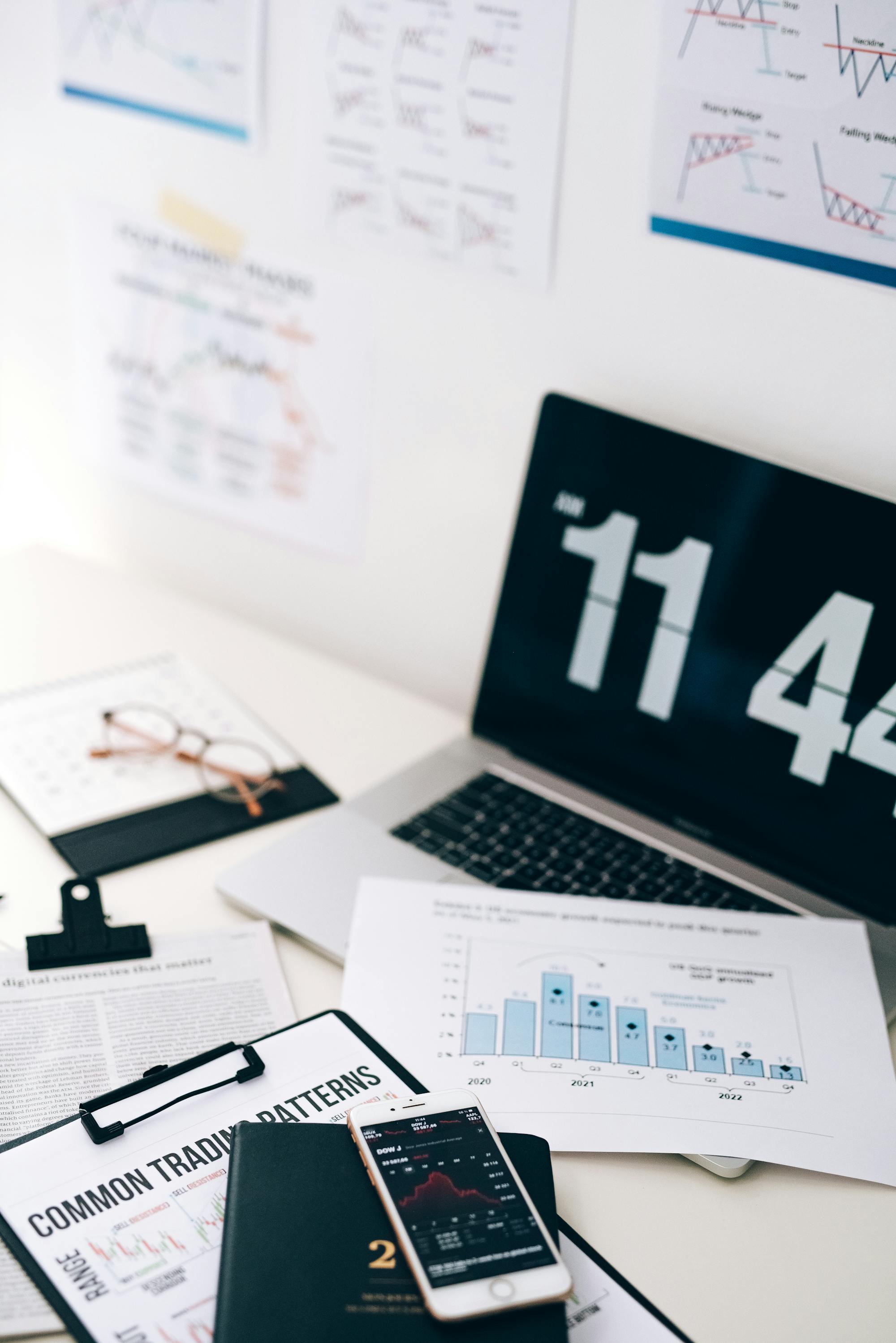 Financial chart on smartphone next to laptop and printed business reports